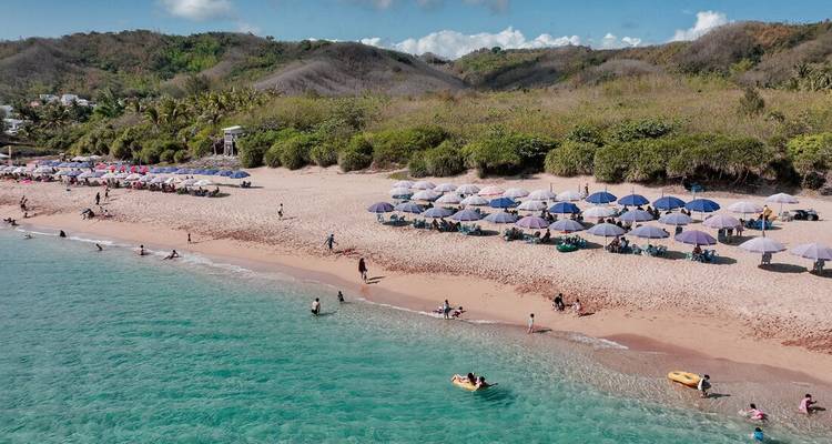 Wide sandy beach with turquoise water, umbrellas and vacationers enjoying the sun