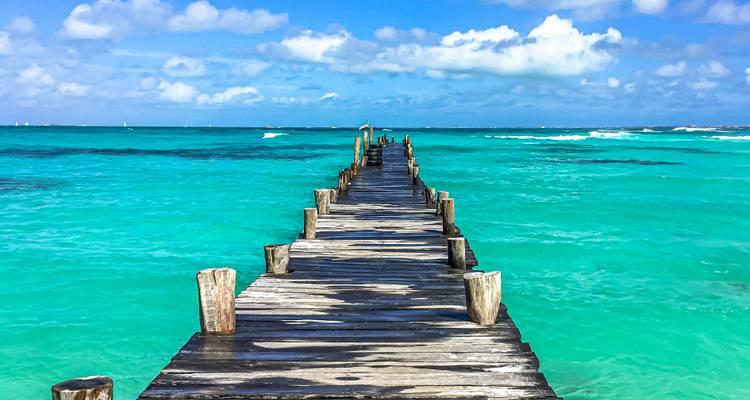Jetée en bois usée par le temps s'étendant dans la mer des Caraïbes d'un turquoise éclatant sous des nuages épars.