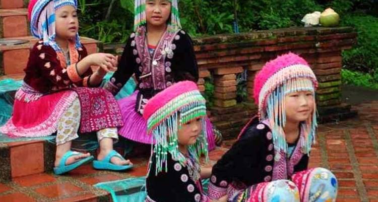 Les jeunes enfants vêtus de costumes colorés des tribus des collines sont assis sur des marches en brique entourées de verdure.