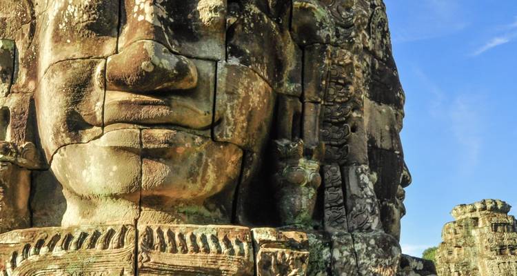 Immense visage de pierre souriante du Temple Bayon baigné dans la lumière chaude de l'après-midi.