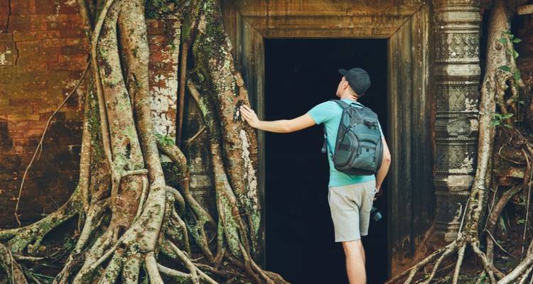 Un routard touche les racines massives d'arbres enveloppant une ancienne porte en pierre au temple Ta Prohm.