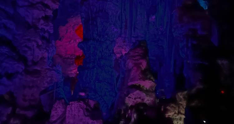 Colorfully lit cavern walls glow in deep blues and pinks inside a dark cave.