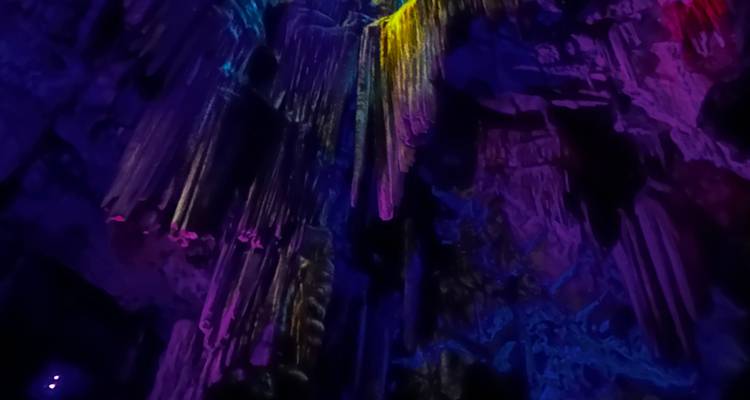 Stalactites in a cave illuminated with purple and yellow theatrical lighting.