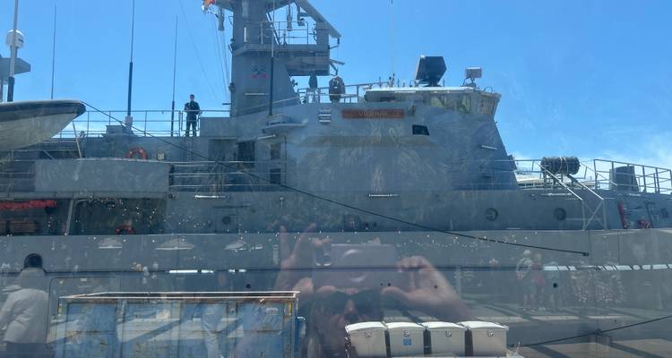 Photo of a naval vessel taken through glass, showing strong reflections including the photographer.