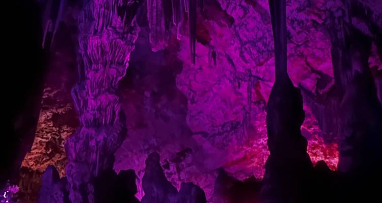 Purple-hued cave chamber with jagged rock formations lit by colored spotlights.