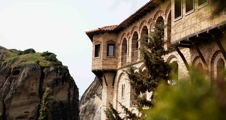 Stenen klooster met boogvensters op een kliffrand met groen eromheen in Meteora.
