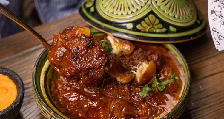 Primer plano de un delicioso tagine de carne marroquí humeante siendo servido desde un plato tradicional.