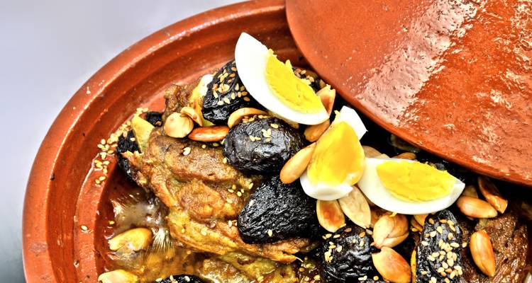 Tajín tradicional cubierto con huevos, aceitunas y almendras dentro de una olla de barro.