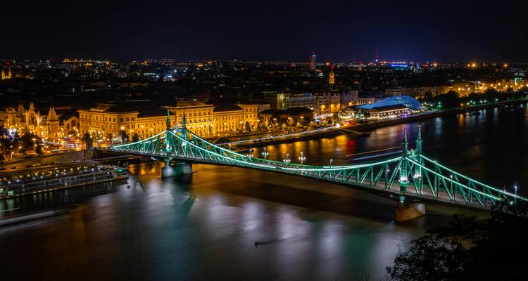 Liberty Bridge glowing green over the Danube with Budapest city lights mirrored in the water