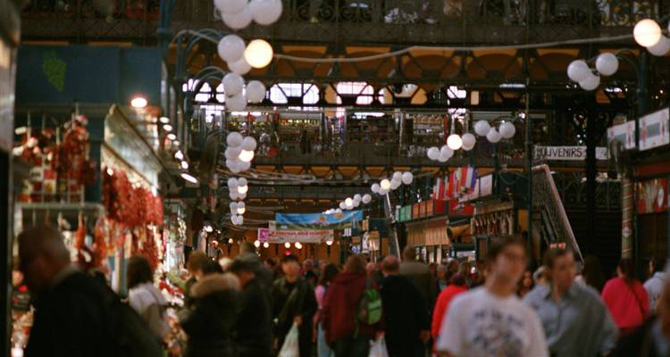 Bustling indoor market hall with colourful stalls and hanging lights crowded with shoppers