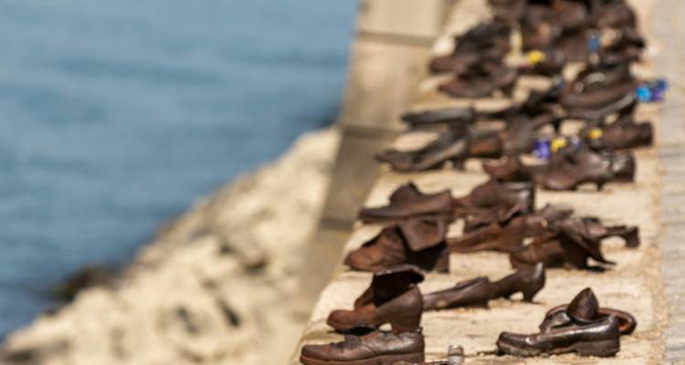 Bronze shoe sculptures lined along the river embankment memorial with water in background