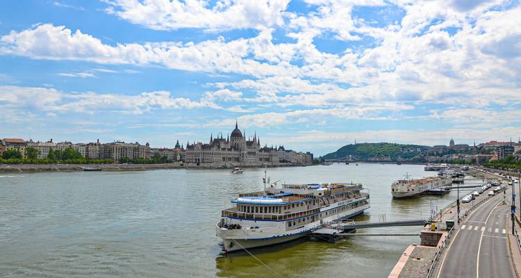 Daytime panorama of Danube River with moored cruise boats and Hungarian Parliament in distance