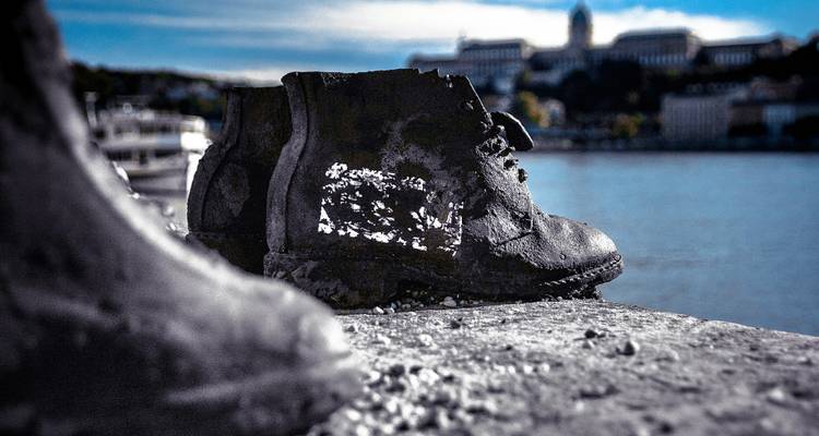 Botte de fer usée du mémorial de l'Holocauste « Chaussures sur le Danube » avec le fleuve et le château flous en arrière-plan.