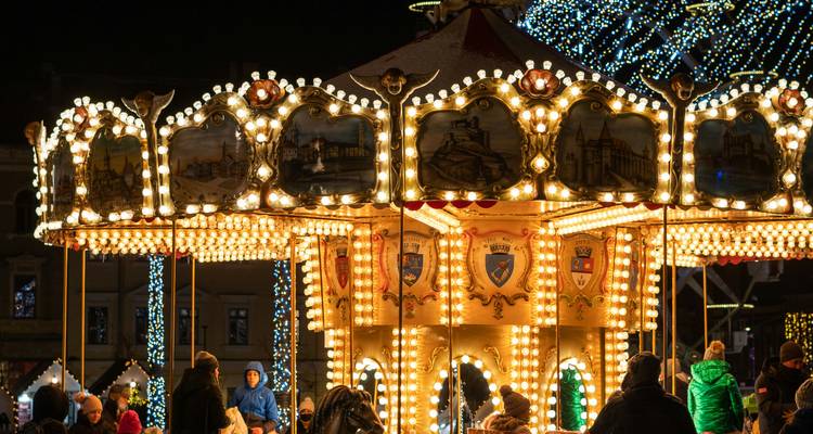 Un carrousel vintage brillamment illuminé s'illumine la nuit au marché de Noël, entouré de visiteurs vêtus chaudement.