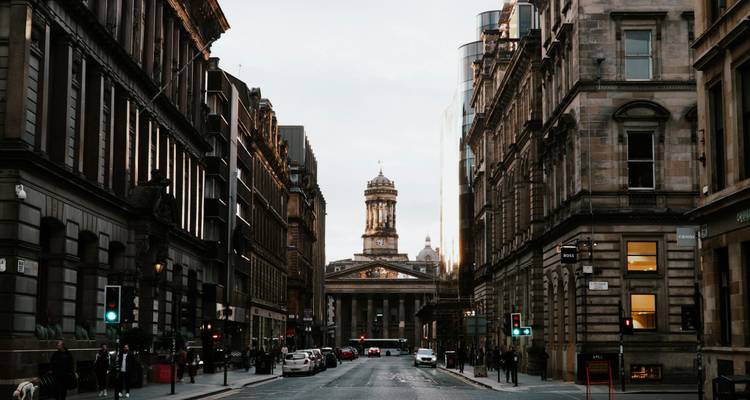 De grands bâtiments victoriens encadrent une rue droite de Glasgow menant à la tour de la Galerie d'art moderne au crépuscule.