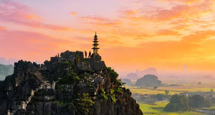 Pagoda recortada contra el cielo en la cima de un pico de piedra caliza afilada que domina extensas llanuras de arroz bajo un cielo al amanecer lleno de colores.