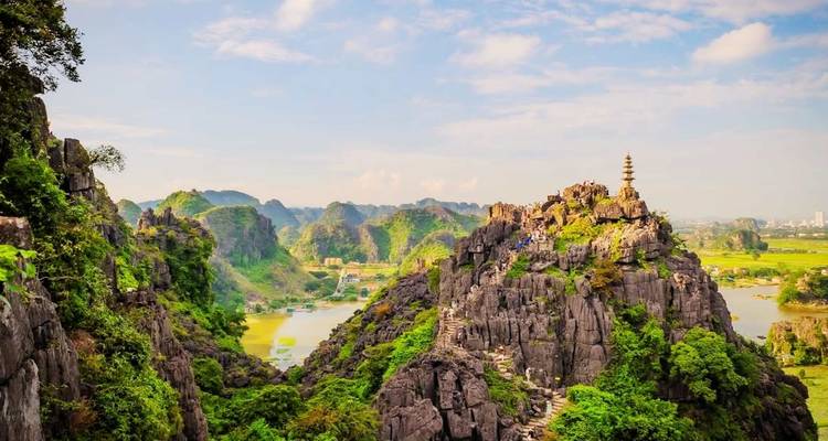 Amplio panorama de acantilados de piedra caliza y arrozales con una escalera de piedra que sube serpenteando hacia un mirador en Ninh Binh.