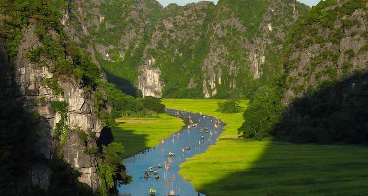 Río estrecho serpenteando a través de un valle de karst verde y escarpado con pequeños botes de remos dirigiéndose río arriba.
