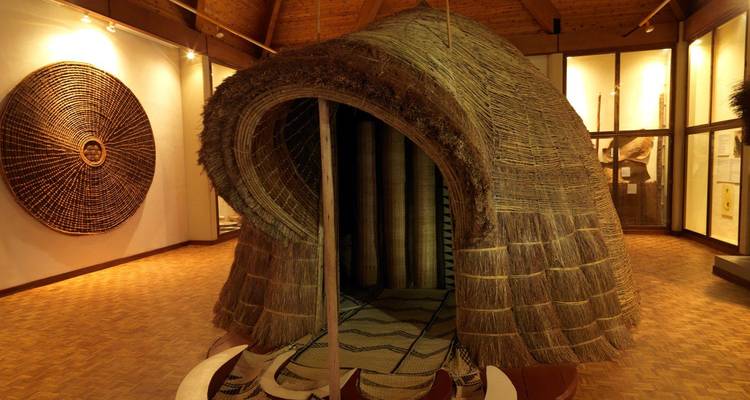 Tentoonstelling van een traditioneel geweven Rwandese koninklijke hut die in een museumgalerie wordt getoond.