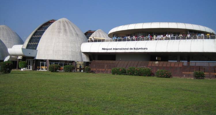 Modernist concrete domes and curved terminal building of Bujumbura International Airport amid a green lawn under clear skies.