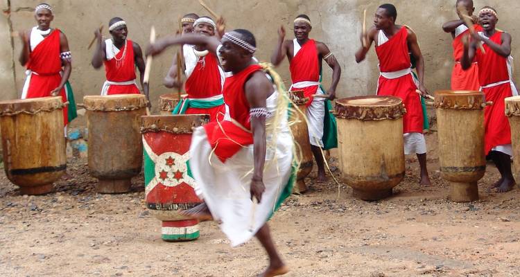 Traditional Burundian drummers dressed in red and white perform energetic rhythms in front of large wooden drums.