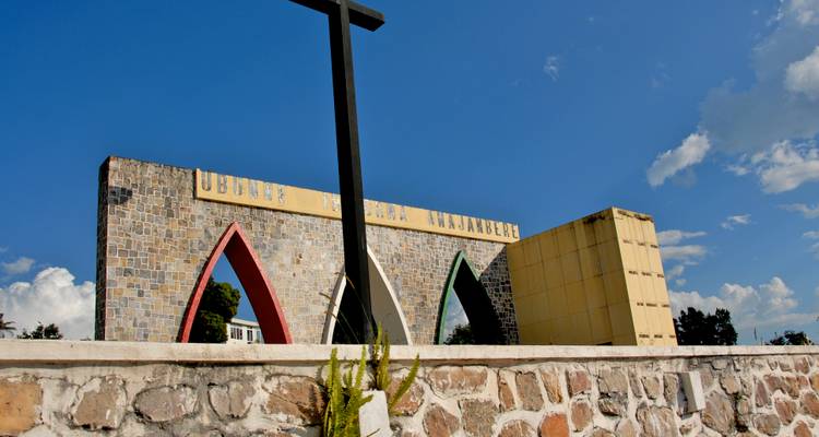 Stone Independence Monument with three coloured arches and a tall cross set against a vivid blue sky.
