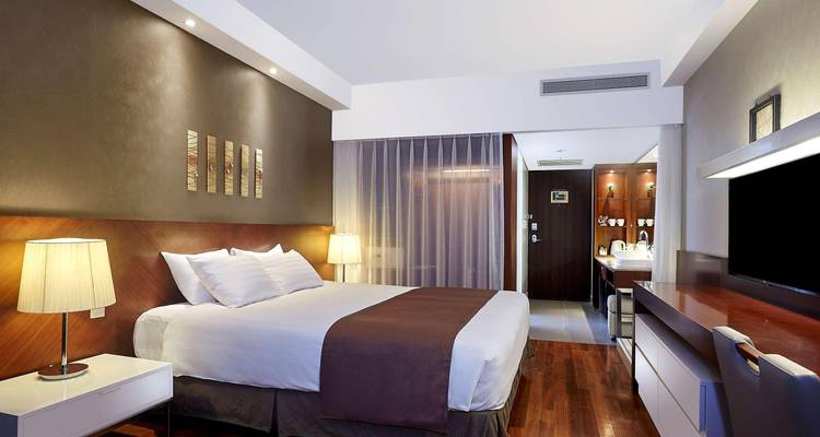 Modernes Hotelzimmer mit warmer Beleuchtung, Kingsize-Bett, Holzakzenten und minimalistischer Einrichtung.