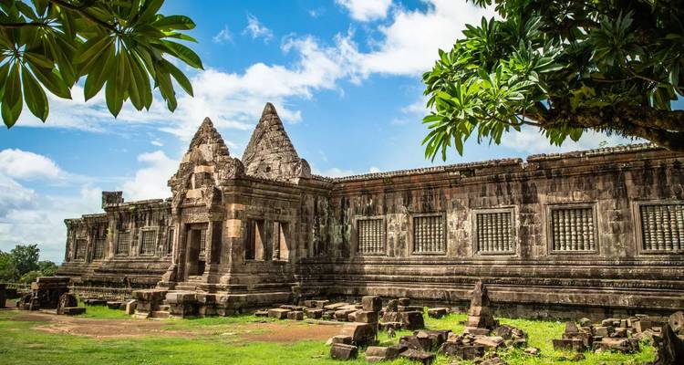 Ruines de pierre du Wat Phou disposées sur une pelouse verte sous un ciel tropical radieux.