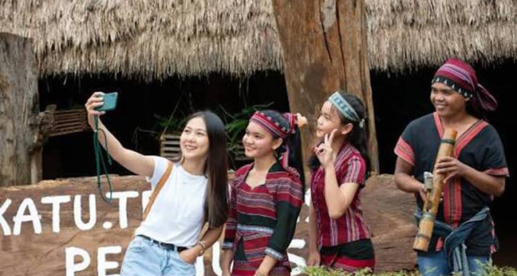 De jeunes voyageurs vêtus de vêtements traditionnels des tribus des collines prennent un selfie devant une maison au toit de chaume.