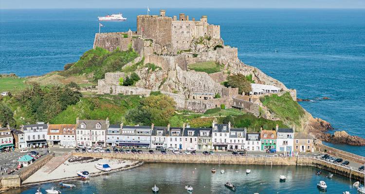 Luchtfoto van het middeleeuwse kasteel Mont Orgueil bovenop een rotsachtige heuvel met uitzicht op een charmant havendorpje