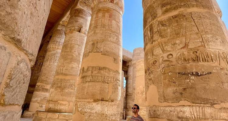 Le voyageur se tient parmi les gigantesques colonnes de grès sculptées d'un temple égyptien antique sous un ciel bleu éclatant.