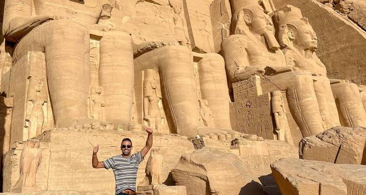 Un visiteur pose avec enthousiasme devant les statues colossales d'Abou Simbel sculptées dans la falaise.