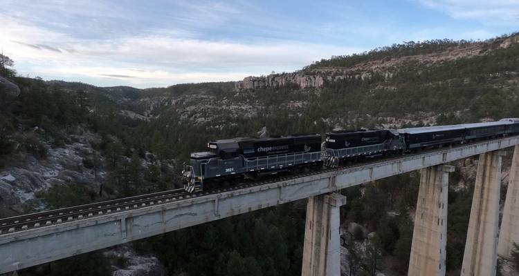 Les locomotives du Chepe Express serpentent sur un haut pont au milieu de parois de canyon rocheuses à la tombée de la nuit