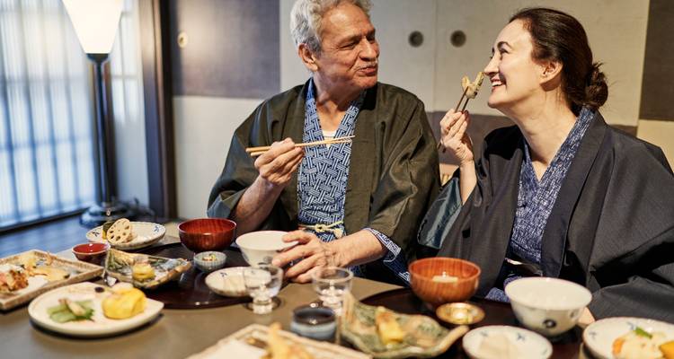 Un couple de personnes âgées vêtu de yukata savoure un dîner japonais traditionnel, souriant devant un assortiment de petits plats et de tasses de saké.