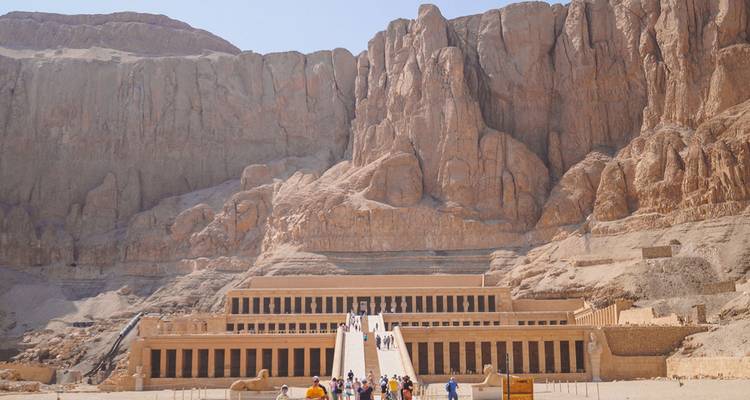 Templo de Hatshepsut construido en acantilados imponentes con turistas acercándose a las grandes escaleras