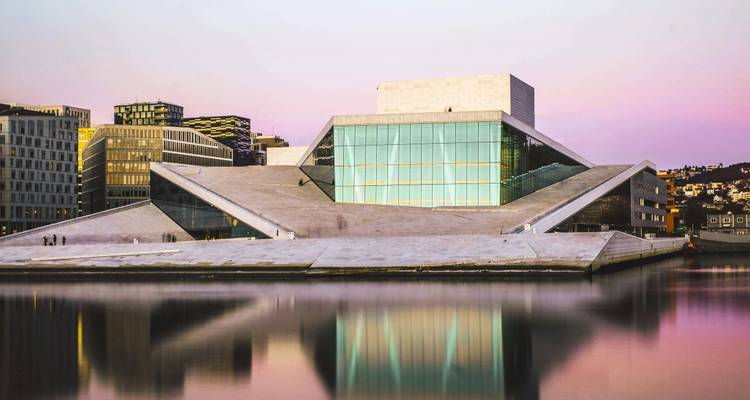Twilight view of Oslo Opera House with pastel sky and mirror-like water reflections.