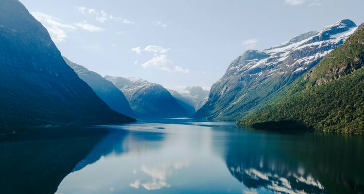 Crystal clear fjord reflecting surrounding snowy mountains under blue skies.