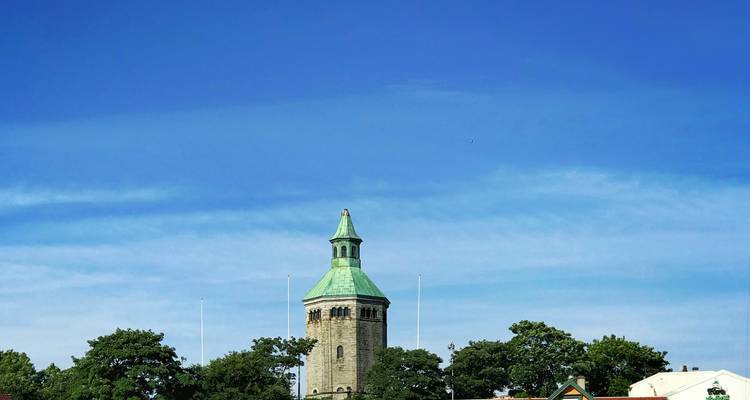 Stone tower with green copper roof rising above treetops against a vivid blue sky.