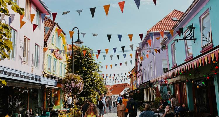 Vibrant pedestrian street lined with pastel houses and bunting flags bustling with shoppers and café patrons.