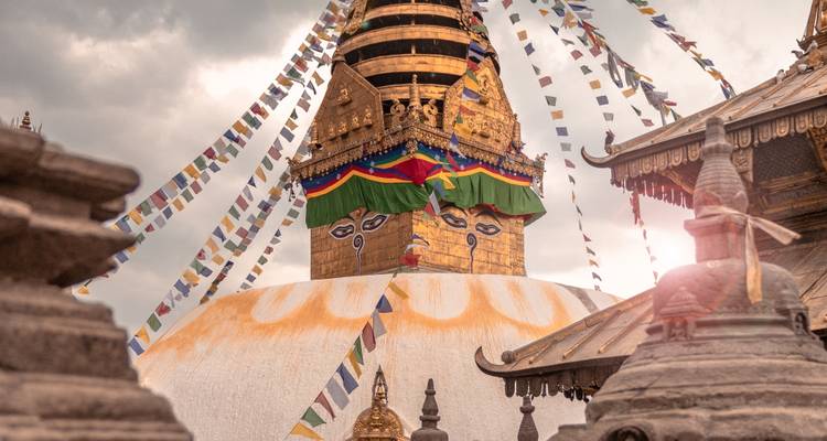 Gros plan du dôme du stupa doré avec des drapeaux de prière colorés s'étendant sur un ciel nuageux dramatique.