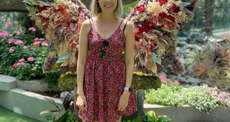 Mujer sonriendo posa frente a una exhibición decorativa de alas de ángel hechas con flores secas.