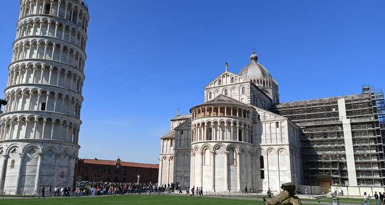 Leaning Tower of Pisa and Pisa Cathedral under clear blue skies with crowds on the lawn.