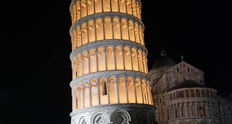 Leaning Tower of Pisa illuminated warmly against the dark night sky.
