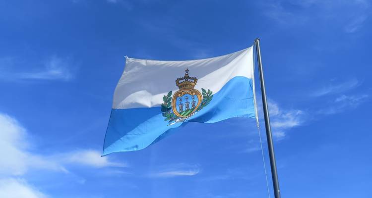 National flag of San Marino waving against a bright blue sky.