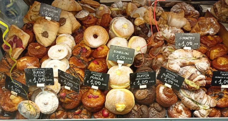 Glass case brimming with assorted Italian pastries and price tags in euros.