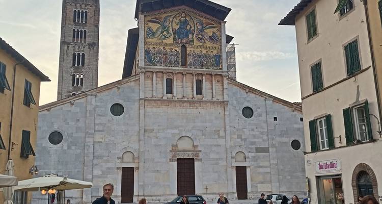 Romanesque church of San Frediano in Lucca with mosaic facade at dusk, surrounded by locals.