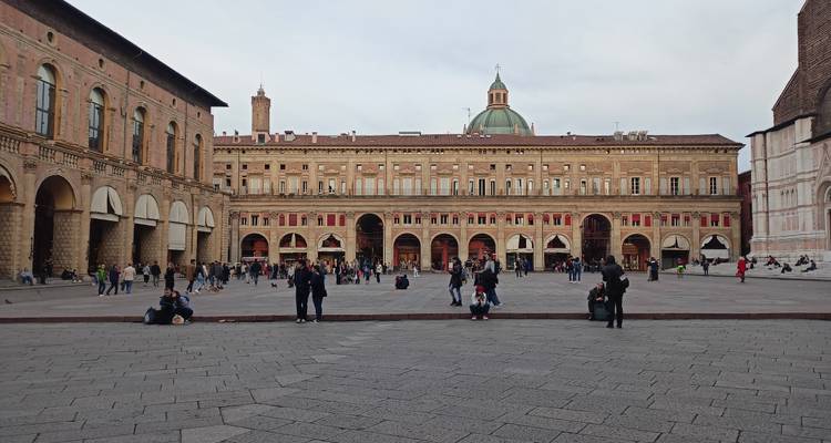 Wide view of Piazza Maggiore in Bologna with people gathered and historic palazzo backdrop.