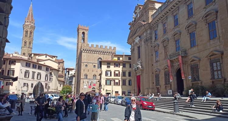 Bustling Florence street scene with medieval towers and tourists under a bright blue sky.