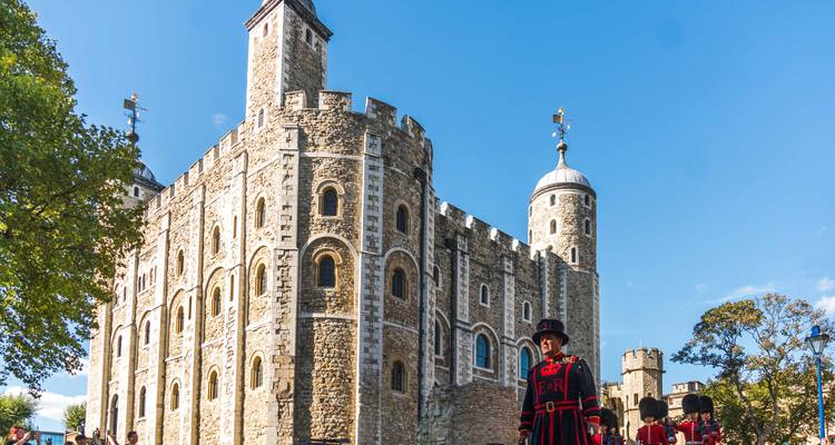 Tower of London battlements with Yeoman Warders and Guards marching under sunny blue sky.