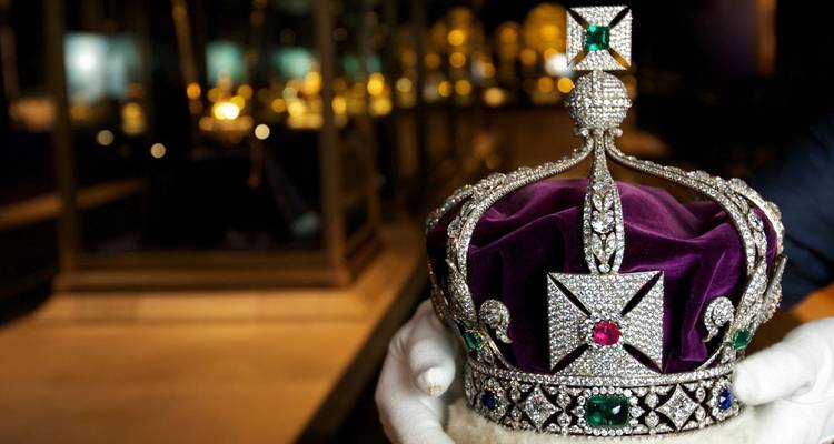 Gloved curator holding the dazzling Imperial State Crown with blurred jewel display cases behind.